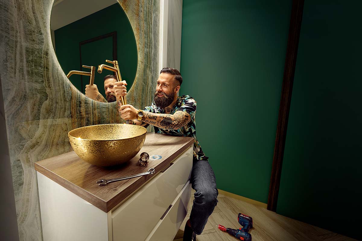 Man installeert gouden kraan op een wastafel in een badkamer