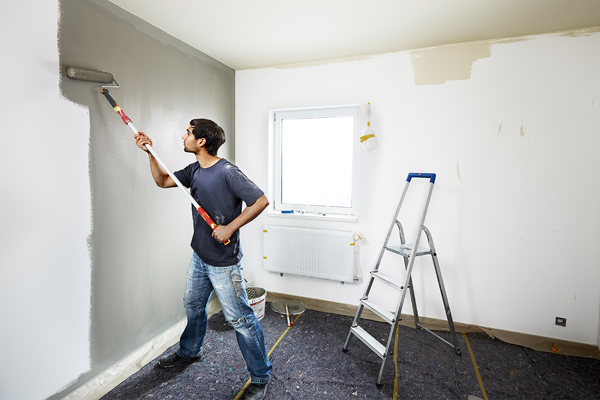 Man schildert muur met verfroller in een te renoveren kamer.