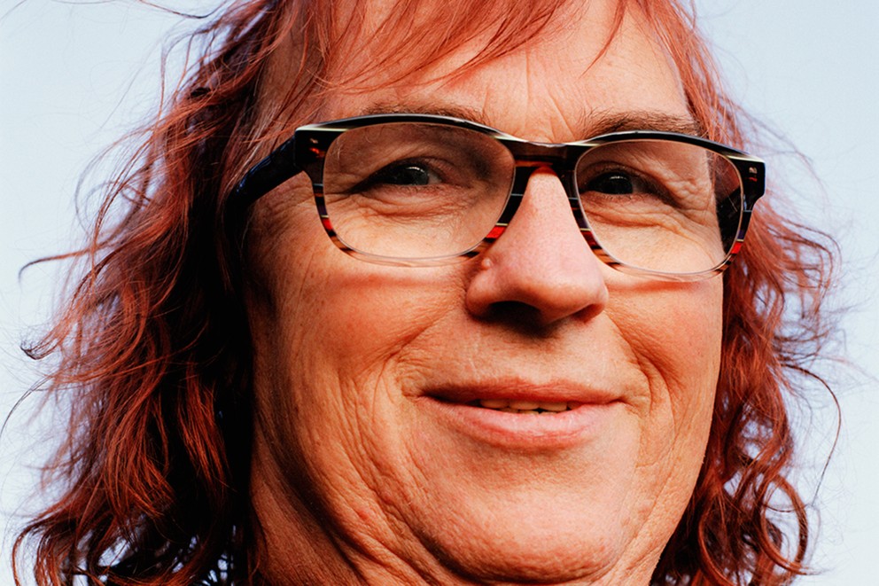 Portret van een lachend persoon met een bril en rood haar