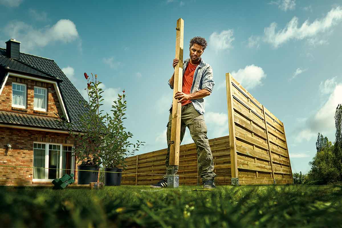 Man plaatst een houten schutting in de tuin.