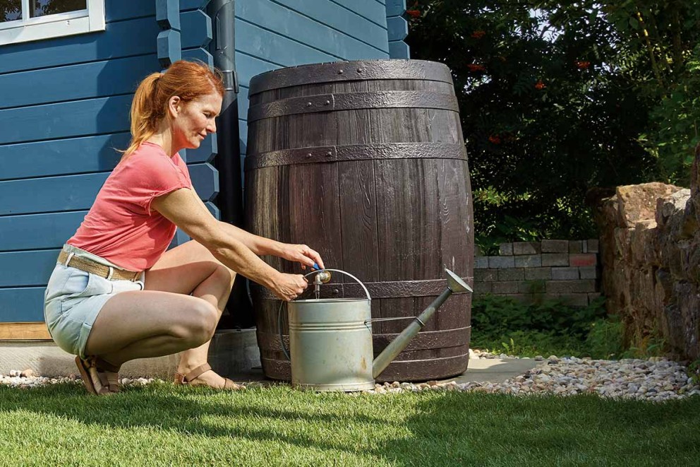 Vrouw vult een gieter bij een regenton in de tuin.