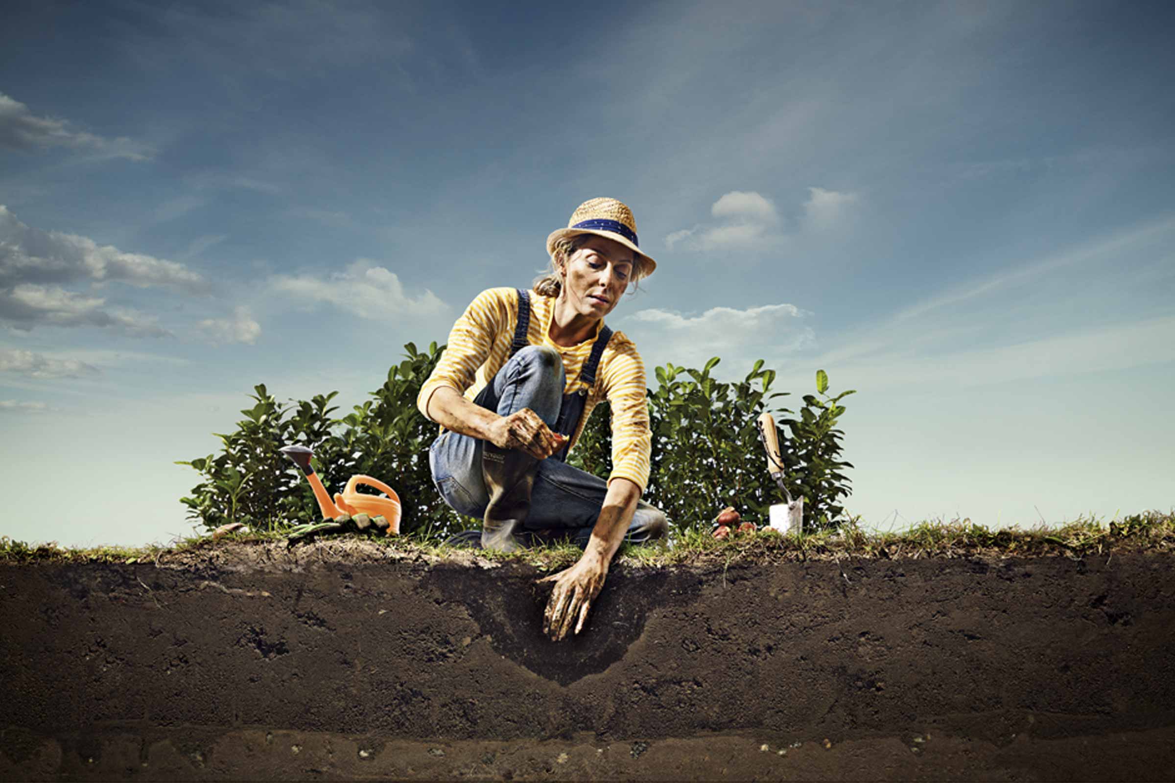 Vrouw plant in de tuinaarde met tuingereedschap zoals een gieter en een schep.