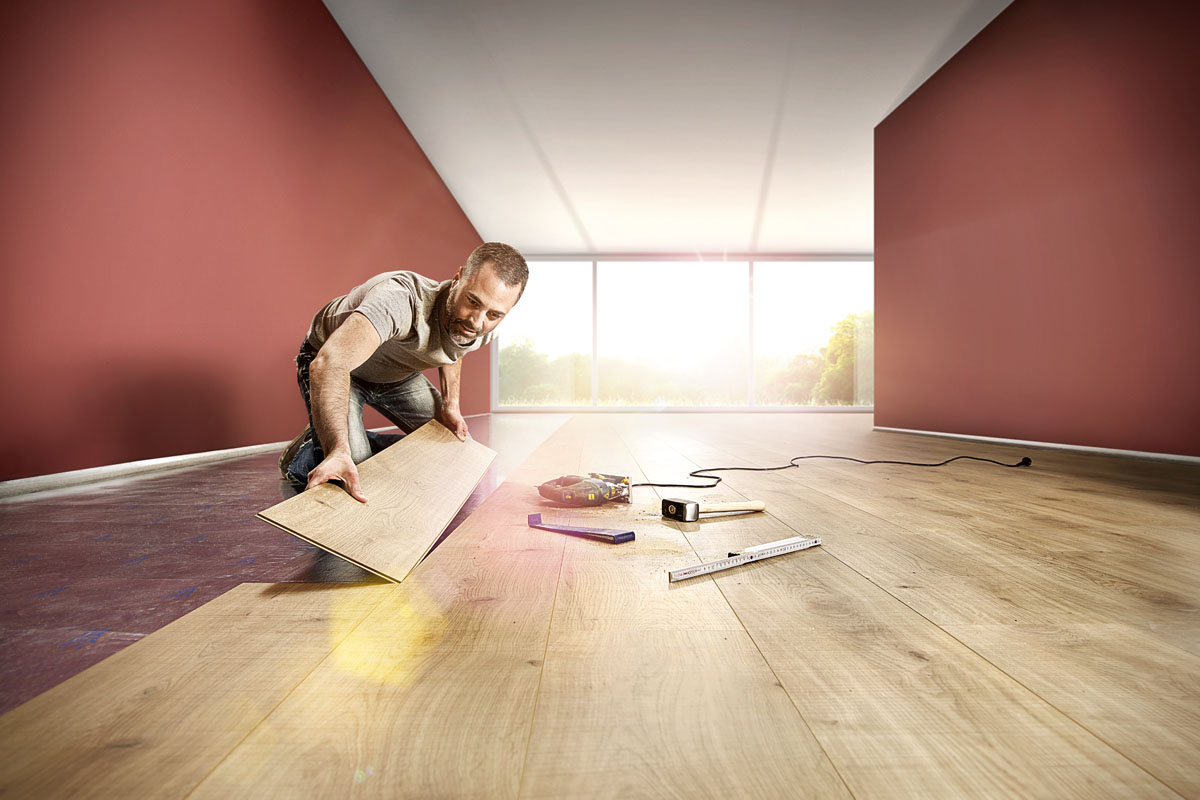 Een man legt laminaat in een lichte kamer met gereedschap