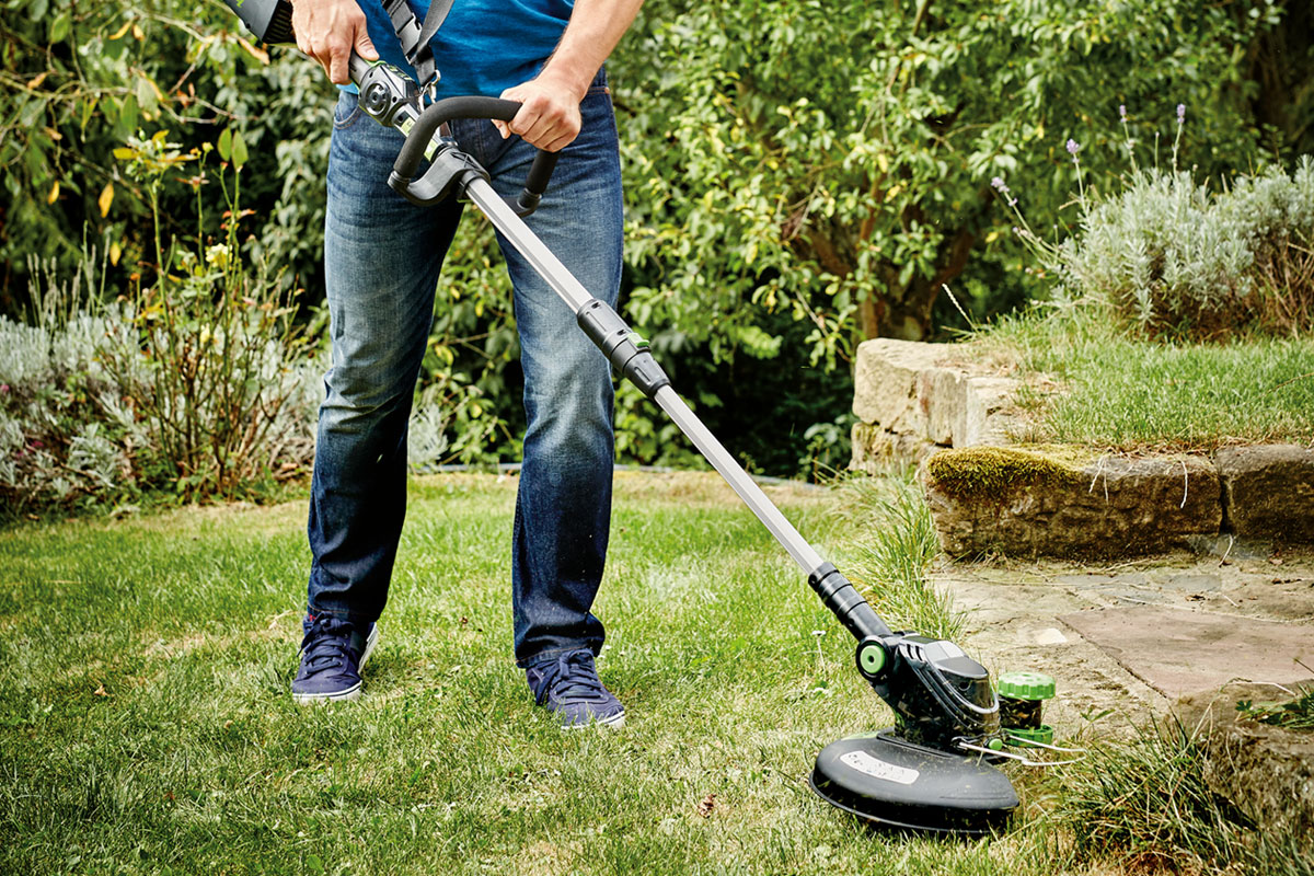 Een persoon gebruikt een grastrimmer in de tuin.