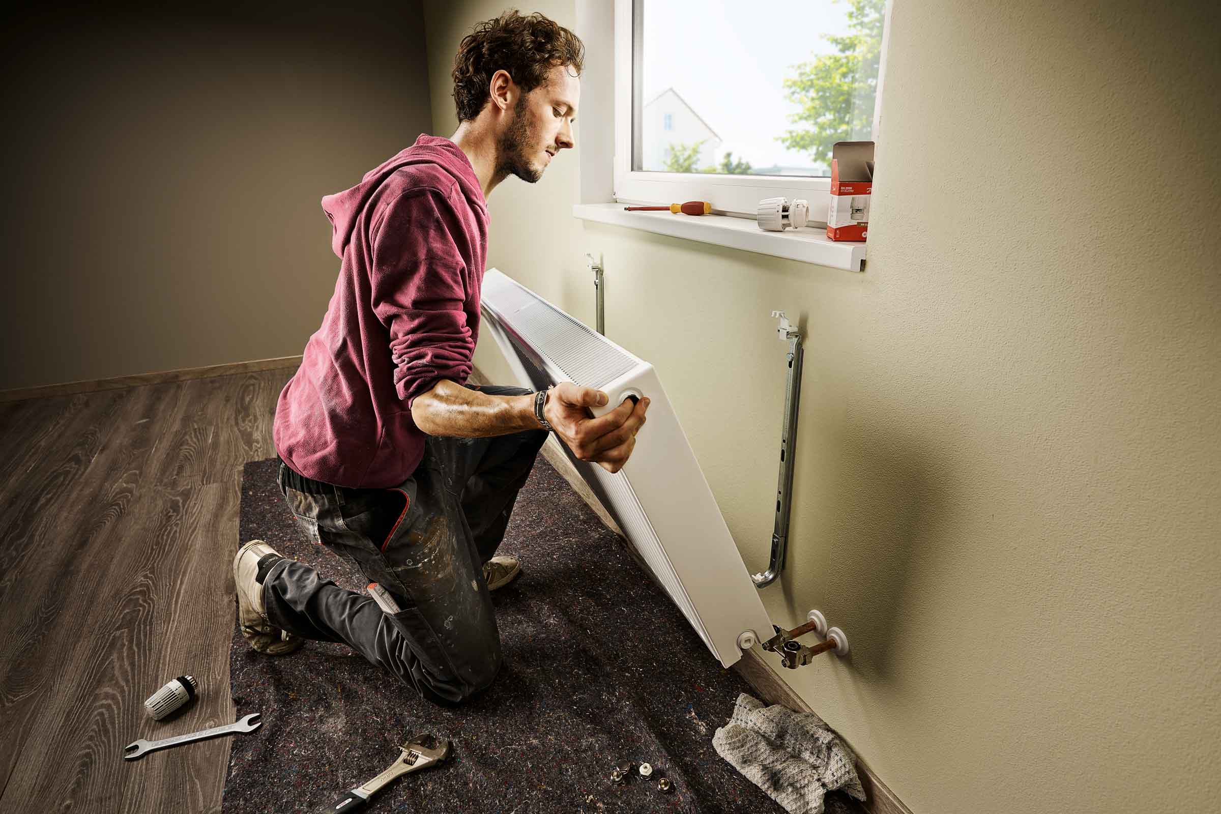 Man installeert radiator aan een muur in een kamer.