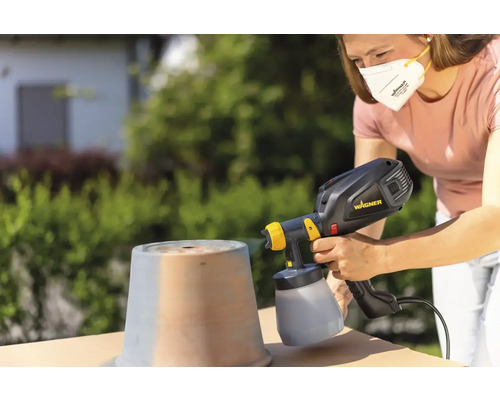 Vrouw spuit pot buiten met verfspuitsysteem