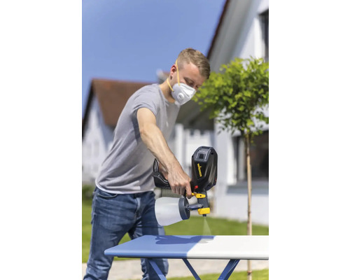 Een man gebruikt een verfspuit om buiten een tafel te schilderen.