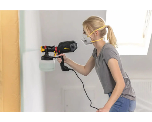 Een vrouw spuit verf op een muur met een verfspuit.