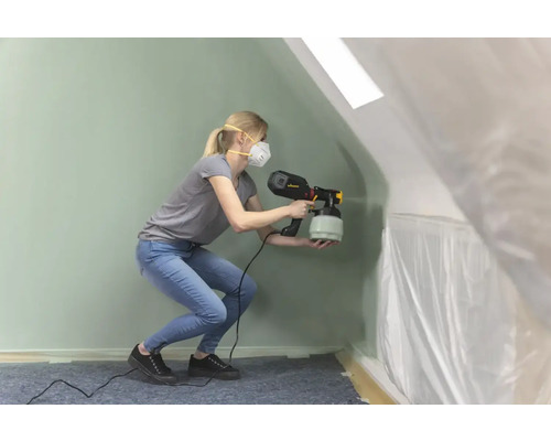 Een vrouw gebruikt een verfspuittoestel in een met folie afgedekte ruimte.