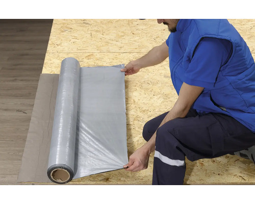 Een persoon rolt een bouwfolie uit op een houten oppervlak.