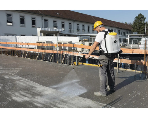 Man gebruikt een rugspuit op een bouwplaats om beton te behandelen.