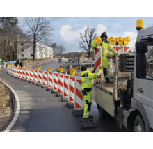 Wegarbeiders plaatsen een rood-witte verkeersgeleiding met waarschuwingslichten op een weg