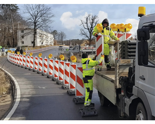 Wegarbeiders plaatsen een rood-witte verkeersgeleiding met waarschuwingslichten op een weg