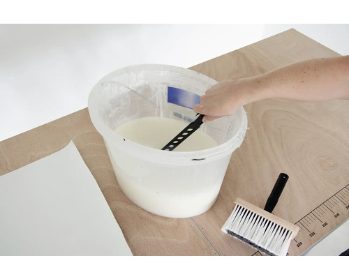 Behanglijm wordt in een emmer gemengd met een roerwerk, ernaast liggen een behangborstel en een behang.