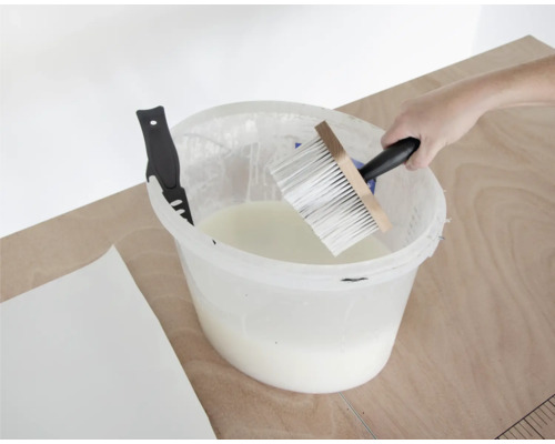 Behanglijm in emmer met kwast en behangmes