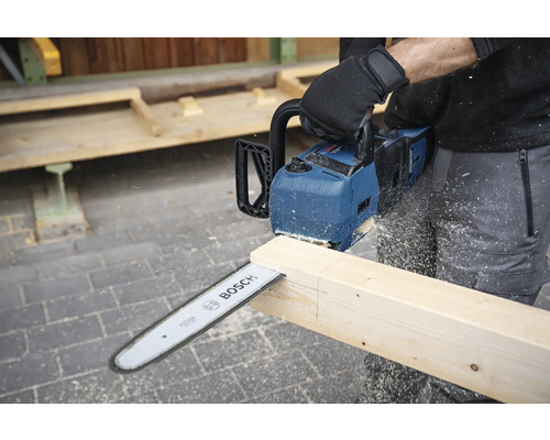 Een persoon zaagt een houten plank met een Bosch accu kettingzaag.