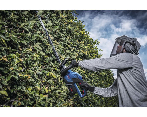 Man met veiligheidsvizier snoeit haag met accu-heggenschaar