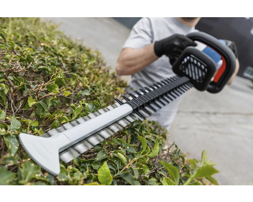 Een persoon snoeit een heg met een heggenschaar.