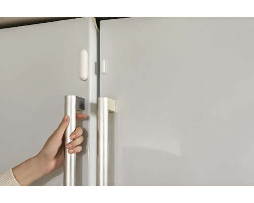 Close-up van een hand die een koelkast opent, voorzien van een deursensor.