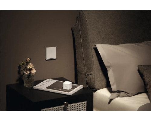 Nachtkastje met decoratie, schakelaar aan de muur en bed op de achtergrond