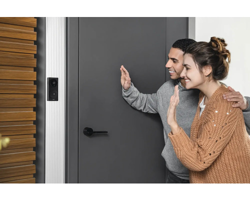 Een paar zwaait voor een voordeur met geïnstalleerde deurbel met camera.