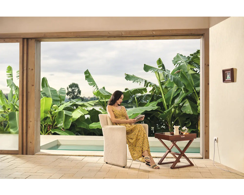 Vrouw zit in fauteuil een boek te lezen, met uitzicht op zwembad en tuin