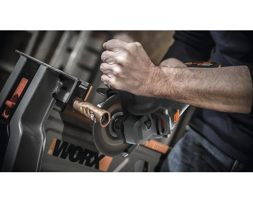 Iemand snijdt een koperen buis door met een doorslijpmachine die in een werkbank is vastgeklemd. WORX logo.