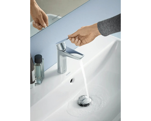 Foto van een wastafel met een lopende kraan en een hand die de kraan bedient