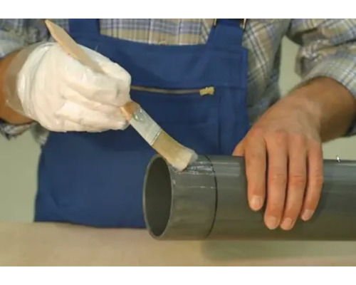 Een persoon brengt met een kwast lijm aan op een grijze buis