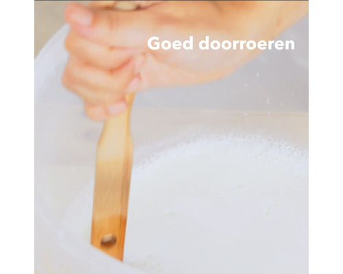 Een persoon roert met een houten stok een witte vloeistof in een emmer