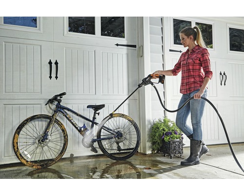 Vrouw reinigt een fiets met een hogedrukreiniger voor een garage.
