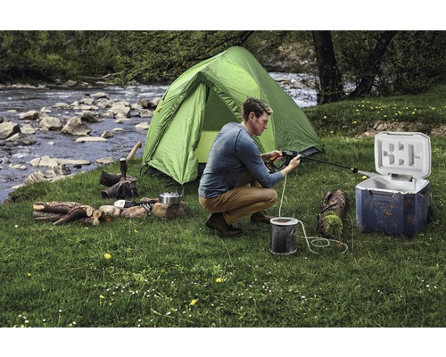 Scène van een kampeeruitrusting met tent, koelbox, brandhout en een persoon die aan het schoonmaken is