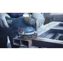 Een persoon schuurt een stuk metaal met een excentrische schuurmachine.