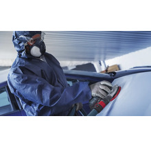 Een man in een beschermend pak schuurt de motorkap van een auto met een schuurmachine.