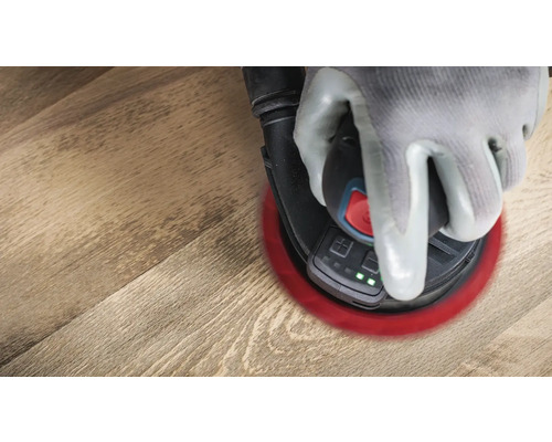 Een hand met beschermende handschoen bedient een excentrische schuurmachine op een houten oppervlak.