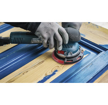 Een vakman schuurt een blauwe houten deur met een excentrische schuurmachine.