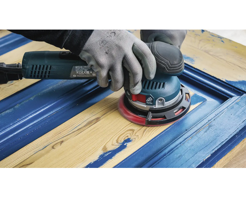 Een vakman schuurt een blauwe houten deur met een excentrische schuurmachine.