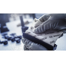 Een hand met handschoen houdt schuurpapier vast op een schuurblok