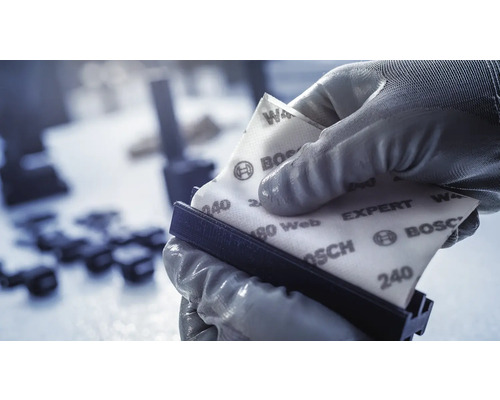 Een hand met handschoen houdt schuurpapier vast op een schuurblok