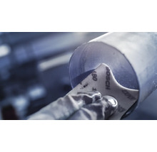 Een arbeider schuurt een metalen buis met schuurpapier korrel 180.