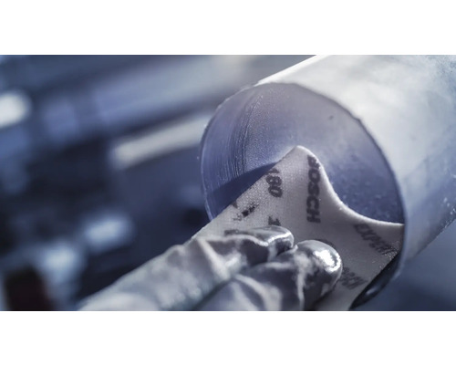 Een arbeider schuurt een metalen buis met schuurpapier korrel 180.