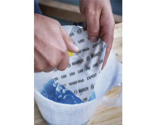 Persoon snijdt Bosch schuurpapier met korrel 180 in een maatbeker