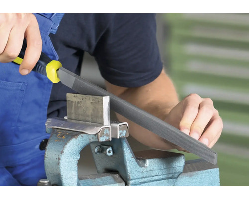 Een werkplaatsscène toont een man die een metalen vijl met handvat gebruikt om een stuk metaal in een bankschroef te bewerken.