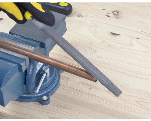 Een bankschroef houdt een koperen pijp vast die met een vijl wordt bewerkt.