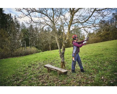 Vrouw met veiligheidshelm snoeit boom met een takkenschaar in een tuin.