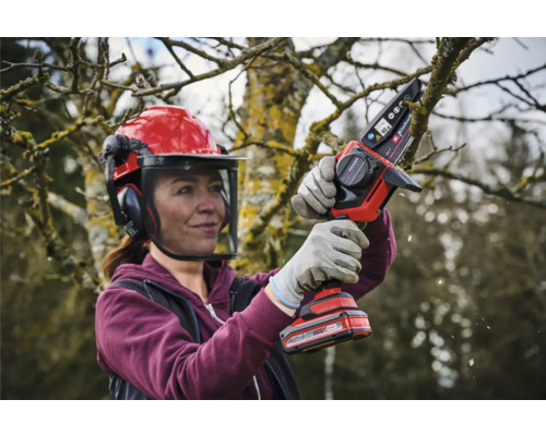 Vrouw met veiligheidshelm en accukettingzaag die een boom snoeit