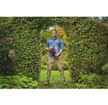 Een man staat in een tuinboog en houdt een accuheggenschaar vast.