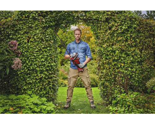 Een man staat in een tuinboog en houdt een accuheggenschaar vast.