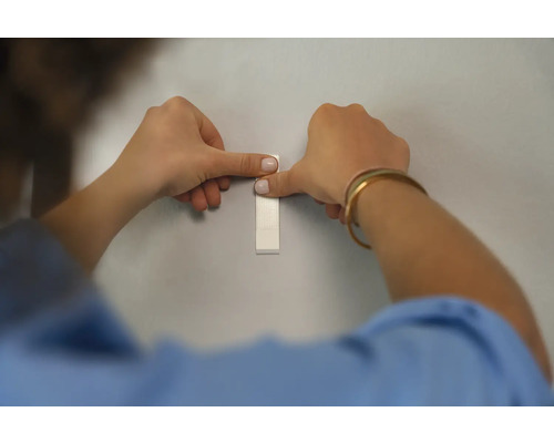 Persoon bevestigt plakstrip aan de muur