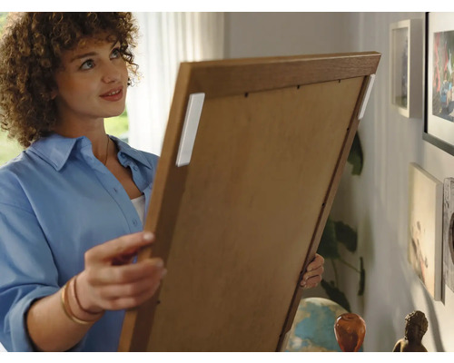 Vrouw bevestigt schilderij met plakstrips aan de muur